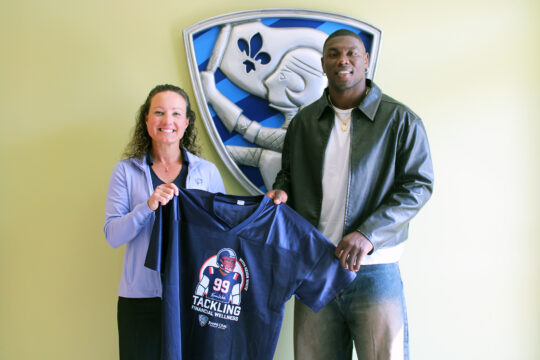 Jeanne D’Arc Credit Union President and CEO Larissa Thurston and New England Defensive End Keion White hold a commemorative jersey featuring the “Tackling Financial Wellness” initiative logo.
