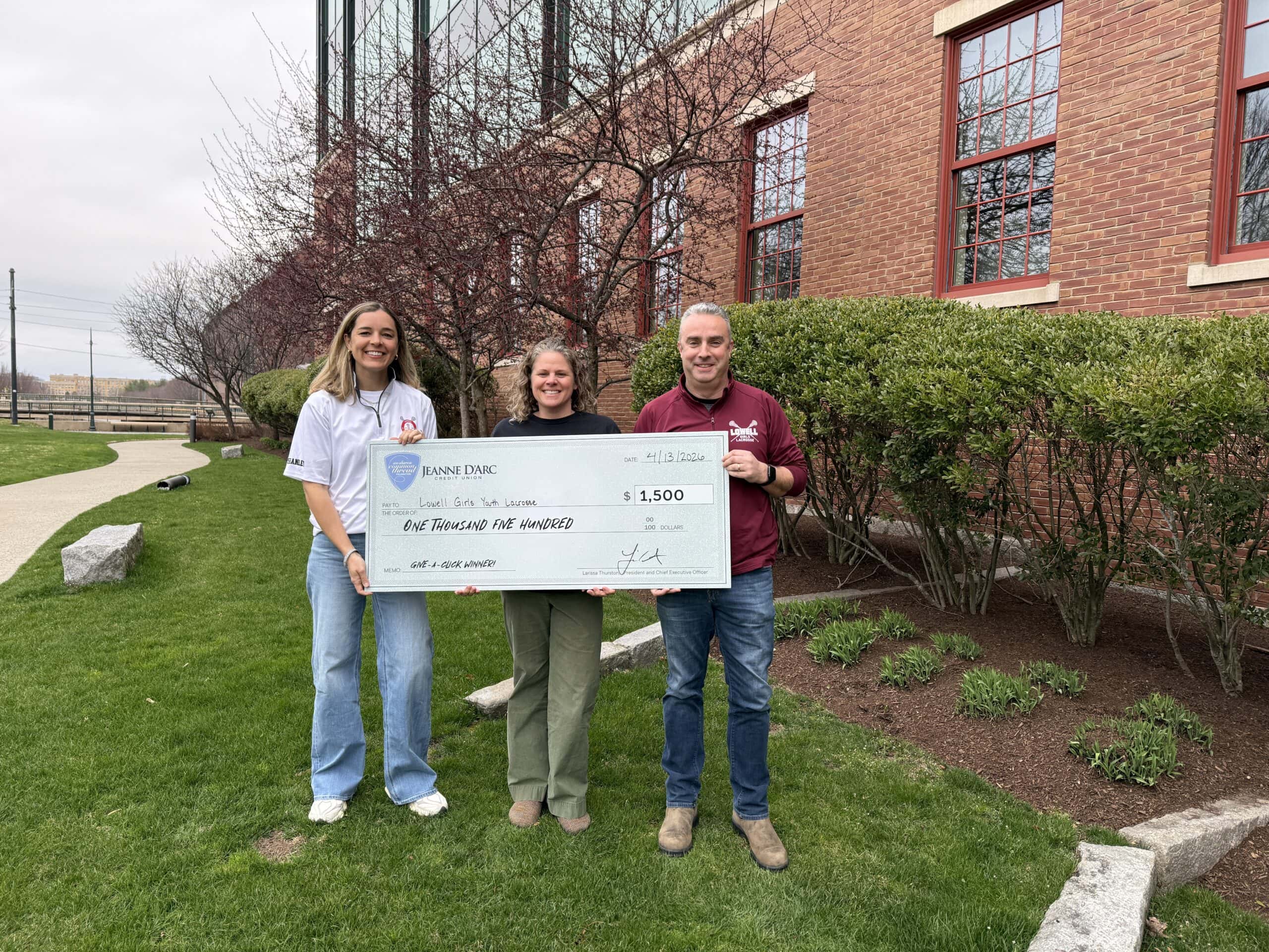 Katie Shanley, President; Christin Monaghan, Board Member; and Jerry Murphy, Coach; from Lowell Girls Youth Lacrosse accept a $1,500 check from Jeanne D’Arc Credit Union for being the Q1 2026 winner of the Give-A-Click campaign on April 13, 2026.