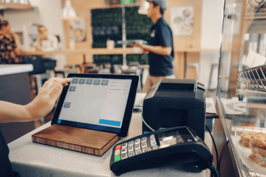 Closeup of the checkout of a small business from the point of view of the cashier. In the background you can see people enjoying the cafe.