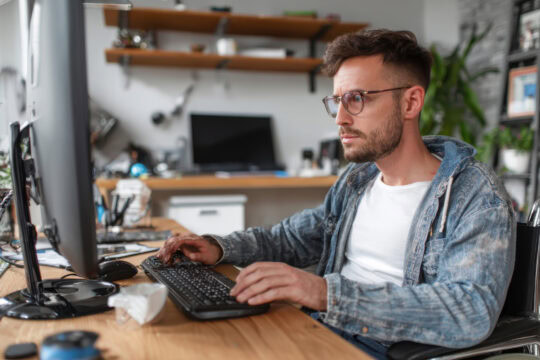 A man in a wheelchair works at his computer at home.
