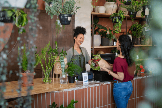 A Black woman assists a customer at the register of her flower shop.