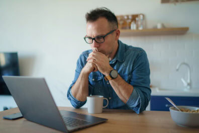 A white man with salt & pepper hair and black framed glasses staring at his laptop with a concerned look on his face.