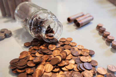 Pennies spilling out of a jar onto a table top. Next to the pile of pennies are paper coin wrappers and small stacks of pennies.