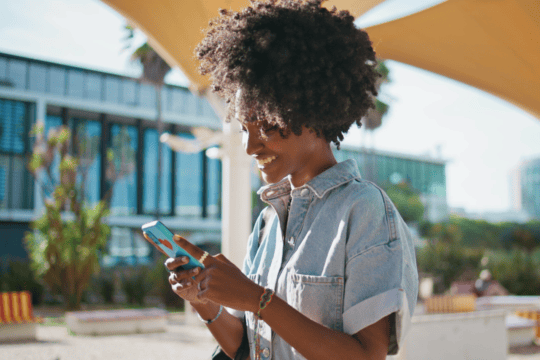 A Black woman with natural hair looks at her cell phone.