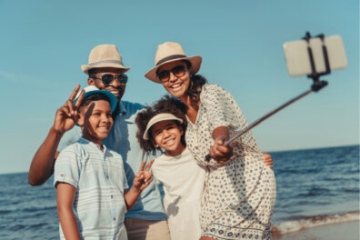 A Black family take a picture on a beach with a selfie stick.