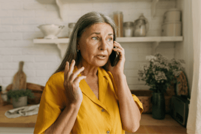 An older white woman has a worried look on her face as she talks to someone on the phone.
