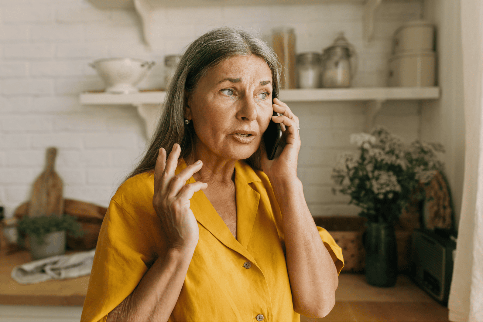 An older white woman has a worried look on her face as she talks to someone on the phone.
