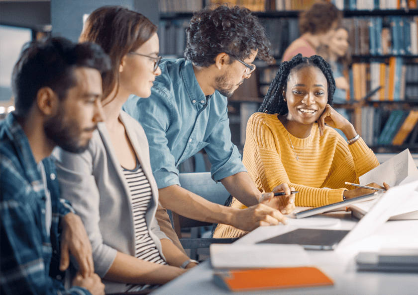 A group of diverse college students smiling while studying in the library.