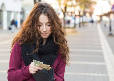A teen saving money by putting cash back into her wallet, instead of spending it.