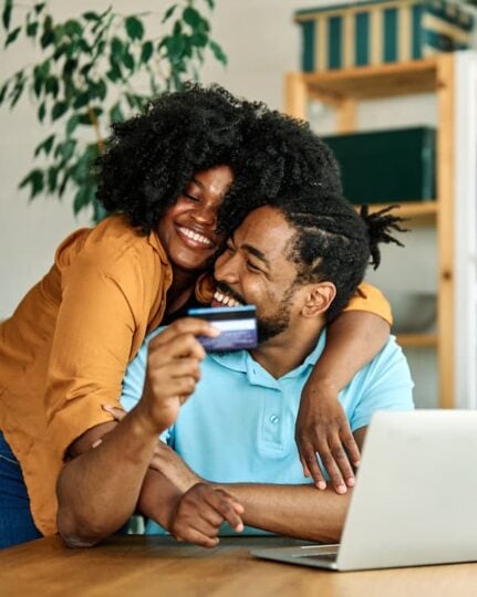 A happy black couple shop online with their JDCU debit card and their MoneyStrong checking account.