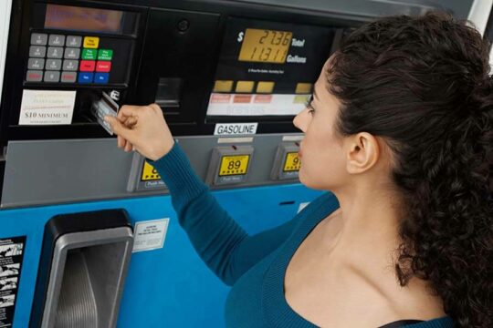 A woman pays at a gas pump using a credit card after checking the machine for a credit card skimmer.