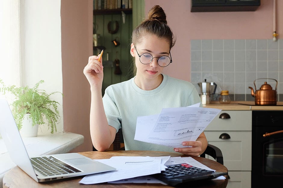 A young woman with a laptop and calculator trying to figure out realistic ways to save money on a lower income.