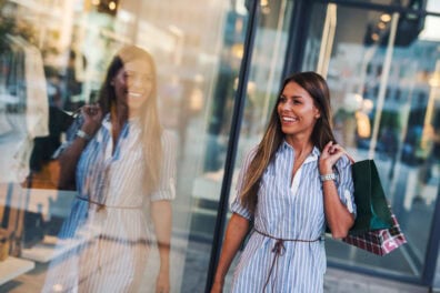 A woman carrying a purchase on her shoulder window shops as she walks down the street.
