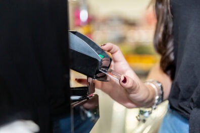 Close up of a woman's hand paying with a credit card at a checkout terminal.
