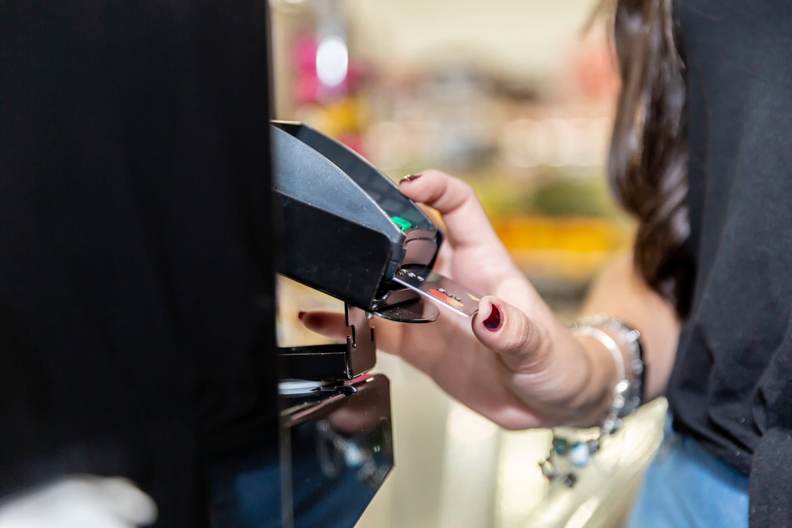 Close up of a woman's hand paying with a credit card at a checkout terminal.