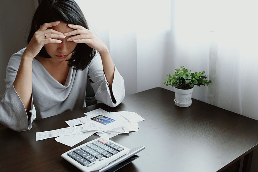 A woman looks down at her bills and credit card and realizes she is overspending.