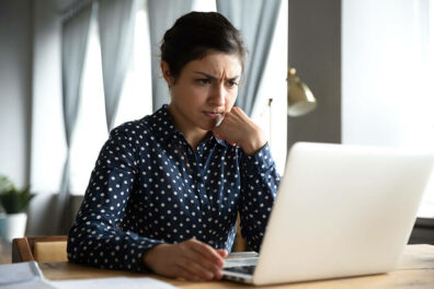 A concerned woman looks at a laptop screen that shows she has a negative bank account.