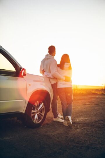 A couple stand next to their white SUV and watch the sun set over the mountains. They were able to rebuild their credit and get a new car thanks to a JDCU Rebuild Auto Loan