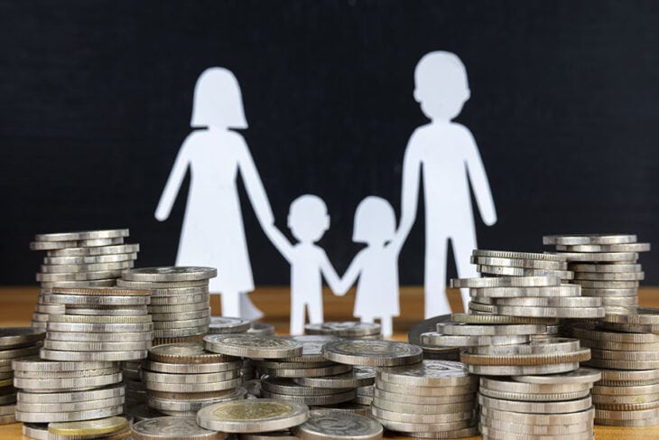 A silhouette of parents and two children holding hands in front of a stack of coins that is growing thanks to a kids savings account.