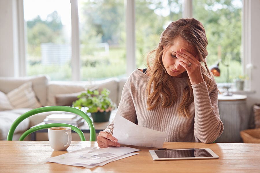 A worried woman reviews her overdrawn account information on her tablet.