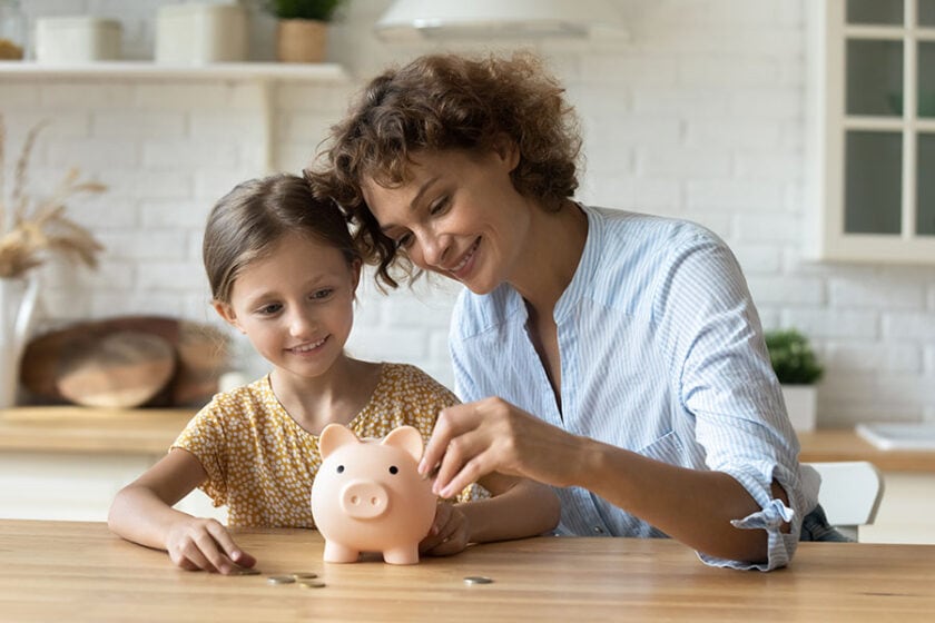 A mother and daughter are enjoying putting coins into a puggy bank as they get ready to open a kids savings account.