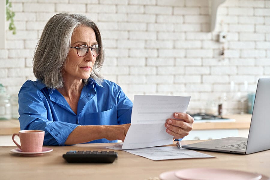 A woman in her 60s sitting in her kitchen reviewing information about Roth vs. traditional IRA accounts.