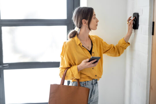 Woman entering a code on her home security system's keypad on her way out the door.