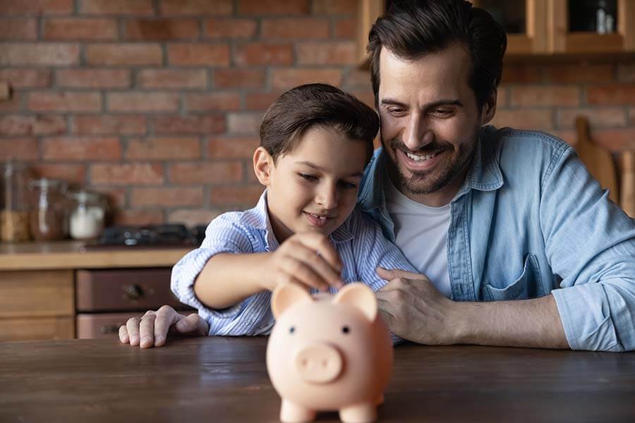 A Dad teaches his son how to save money by putting coins in a piggy bank.