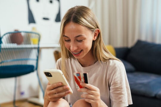 A teenage girl is smart about fraud prevention as she verifies it's a trusted retailer she is purchasing from on her smartphone.