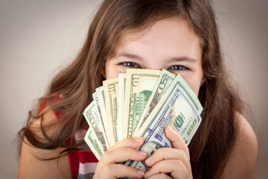 A young girl holds up cash that she has saved to reach her teen savings goals.
