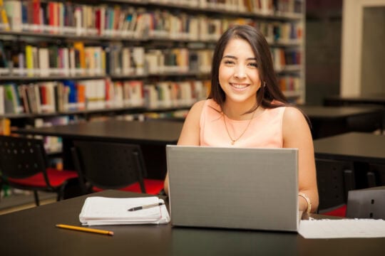 A young college student works on her laptop in the college library.