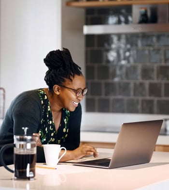 Shot of a smiling young woman using laptop on kitchen counter