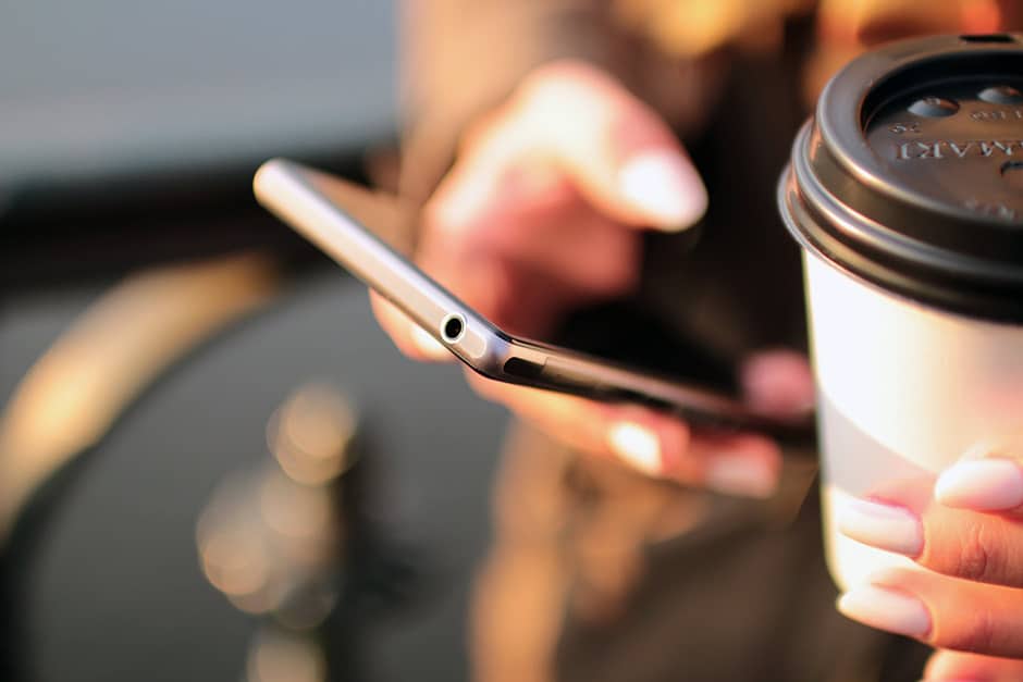 Hand holding a mobile device and a cup of coffee-to-go