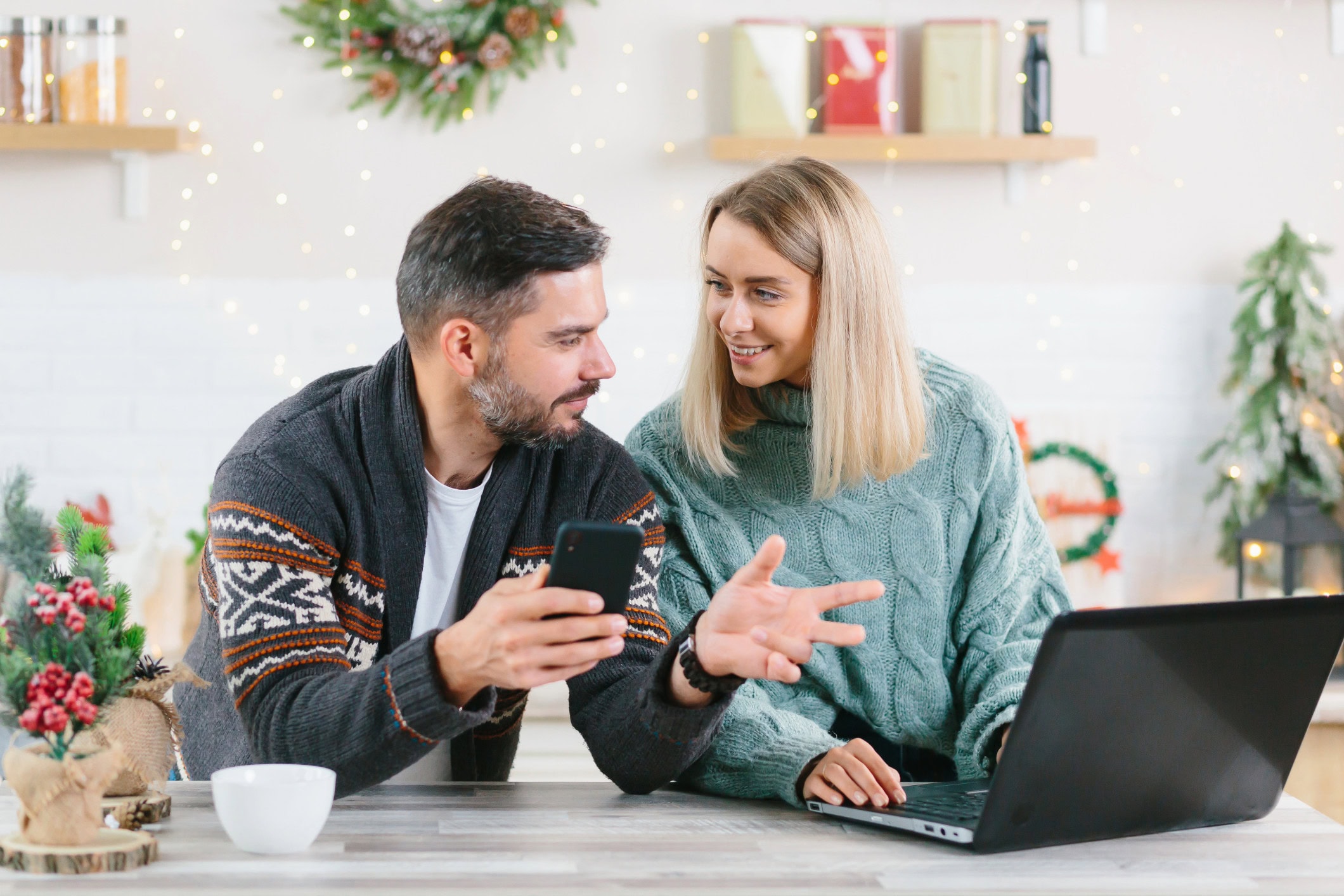 A husband and wife work on their budget together at home. They’re working on their laptop at their kitchen island surrounded by Christmas decorations.