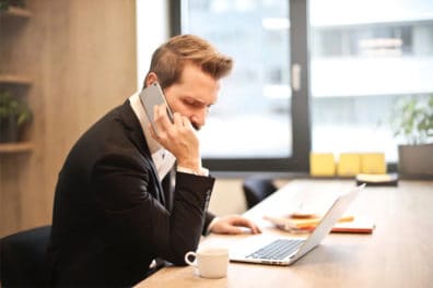 Man sitting at a table on his cell phone and looking at his laptop