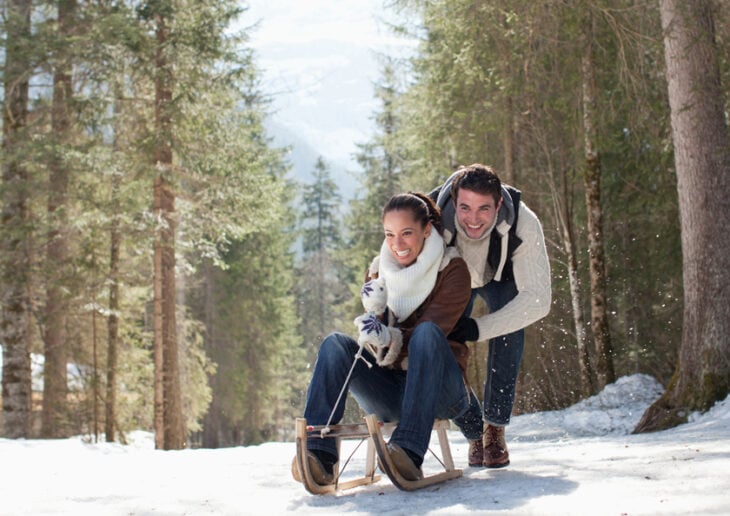 Smiling couple sledding in snowy woods