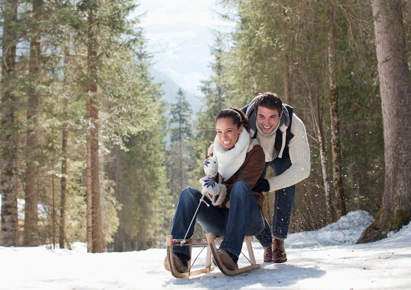 Smiling couple sledding in snowy woods