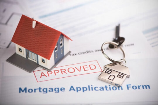 a miniature house and set of keys on top of an approved mortgage loan application