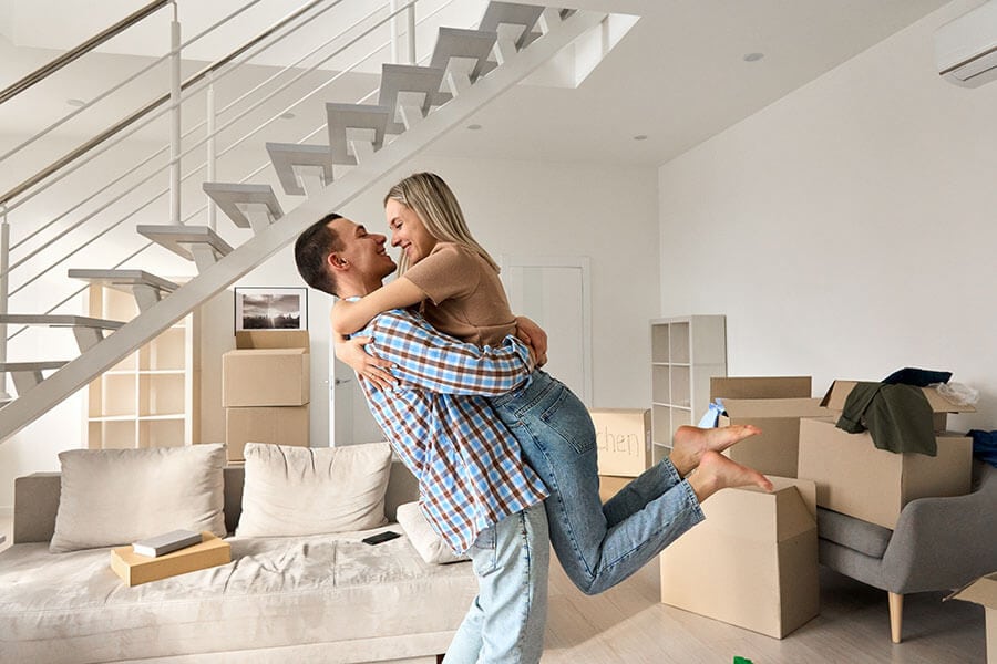 a pair of first-time home buyers hugging happily in their new living room surrounded by moving boxes