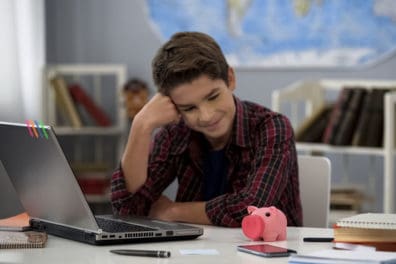 Boy sitting at laptop staring at a piggy bank