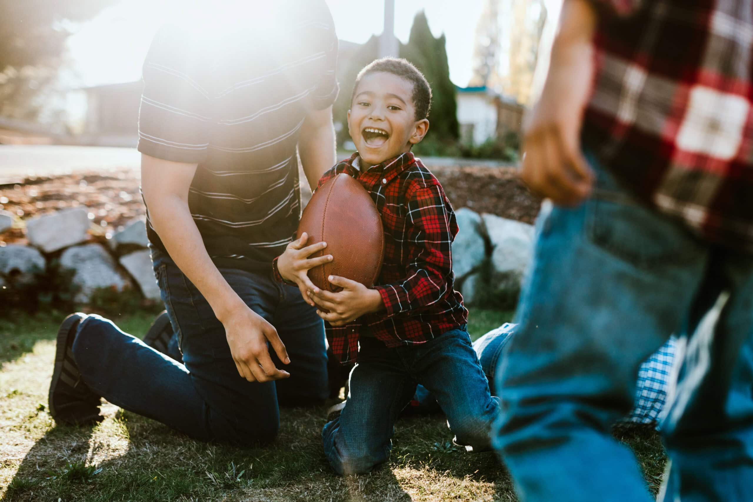 A dad and his three boys play American foot ball in their front yard, having fun spending family time together.