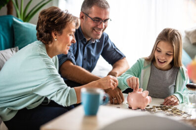 Three generation family putting coins into piggy bank together