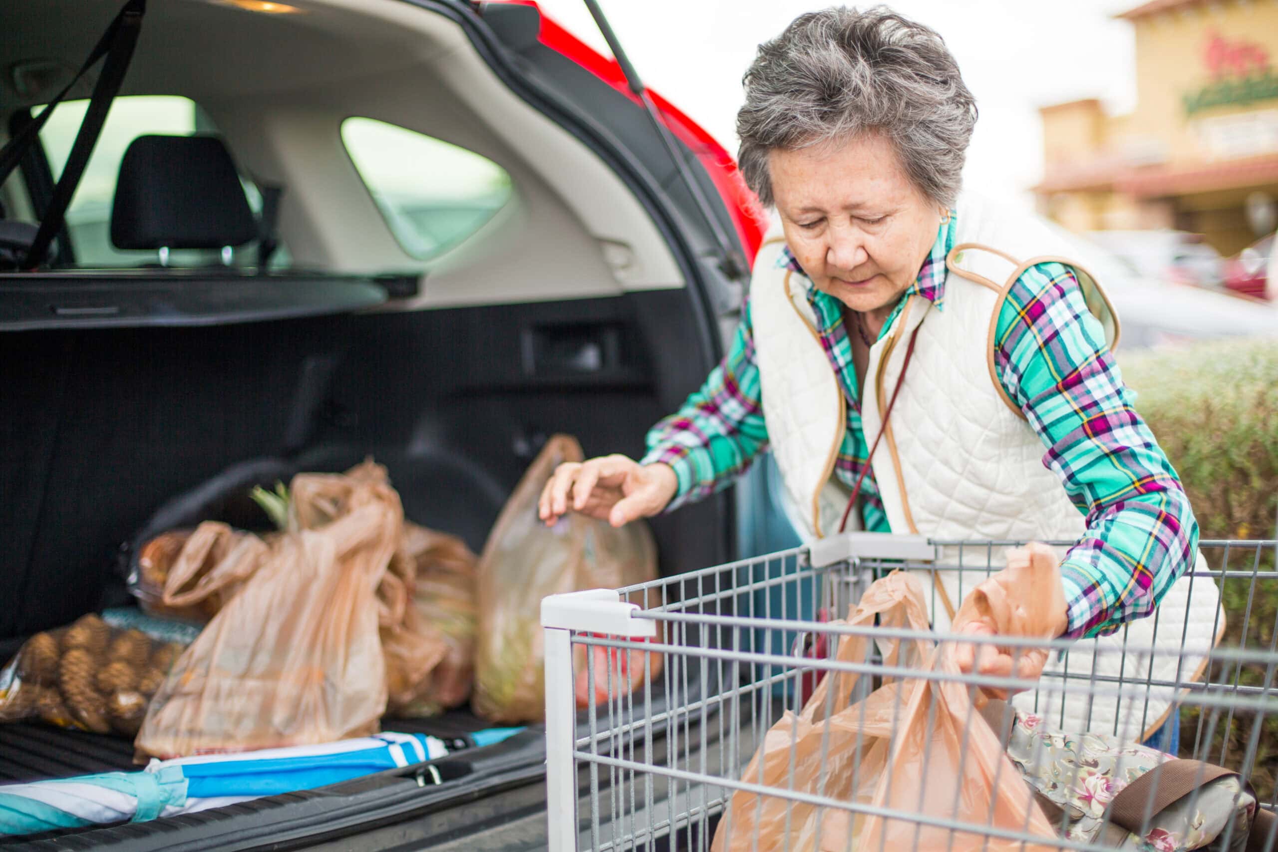 Senior Asian woman loading grocery bags in the trunk of her car.