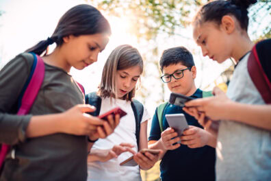 A group of school children stand together looking at their smartphones.