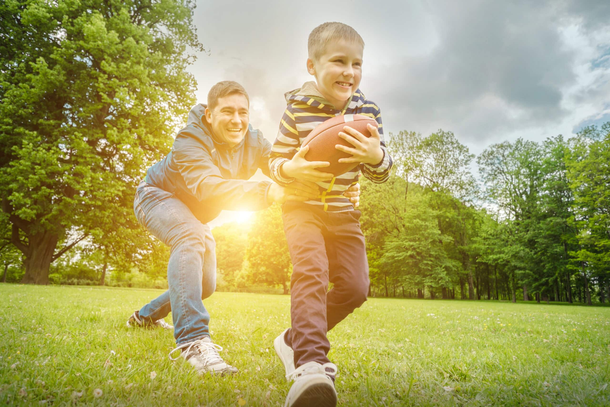 Father and son playing football, Father's day, Playful Man teaching Boy rugby outdoors in sunny day at public park. Family sports weekend.