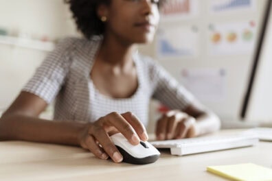 Closeup of a Black woman's hand as she uses a computer mouse.
