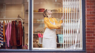 A business owner retracts the security grate in her shop window as she opens for the day.