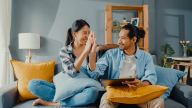 Happy young couple man and woman sit on couch use tablet shopping online furniture decorate home in the living room at new house.