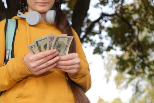 A teenage girl in headphones counts dollar bills.