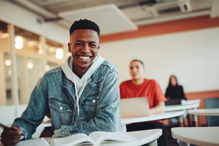 High school student smiling, taking notes in classroom.